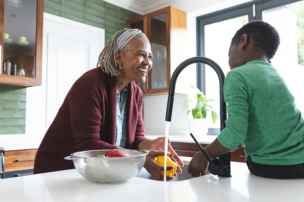 happy grandmother washing in sink smiling to grandson